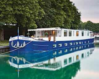 Exterior of a royal-blue bottomed river barge moored alongside a tree-lined canal