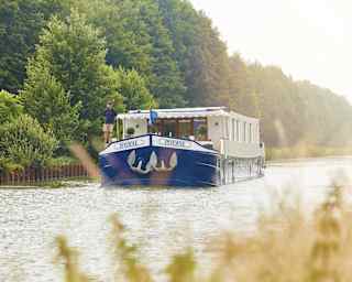 Blue bottomed luxurious river barge sailing along a tree-lined river