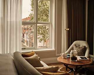 In a Deluxe Room, a window with a view onto a London street spills light on a sofa and chair in soft taupe by a coffee table.