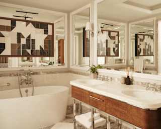 View of a bright mirrored bathroom corner with an egg bath below a mirror with a modern, tiled panel, and a marble twin basin.