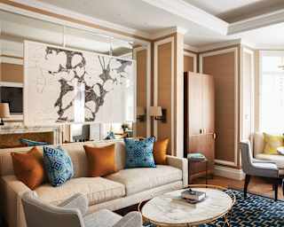 Copper and blue cushions add colour to a large cream sofa in a refined living room with monochrome artwork and marble table