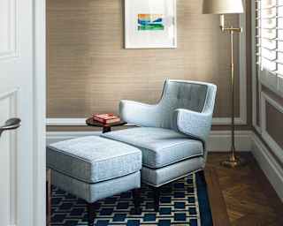 A reading nook with a pale blue armchair and matching ottoman footstool is illuminated by a brass-stemmed standard lamp