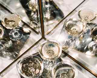 A tray of four Champagne glasses rests on marbled top cornered by mirrored walls which reflect it four ways, seen from above.