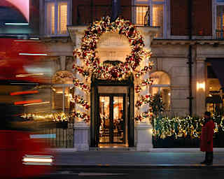 A building entrance decorated with a large, illuminated Christmas wreath, with a blurred red bus passing by in the foreground.