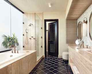 Brushed gold fittings enhance a honey marble vanity, tub and walk-in shower of an elegant bathroom with black floor tiles