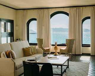 Three Paladian-style arched windows bring dazzling ocean blues into a beige-furnished living area with black floor tiles.