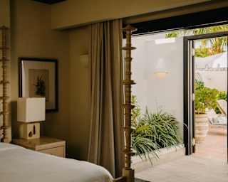 View across a four-poster bed, through open doors to a passage and courtyard beyond, in a five-bedroom private pool villa.