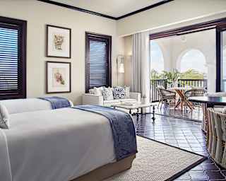 Matching beds with crisp linens and blue throws look out at the sparkling sea of Maundays Bay beyond the private terrace