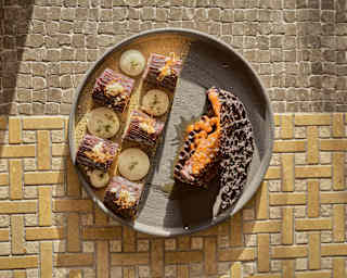 A chocolate mousse dessert with vanilla cream, hazelnut, and pisco ice cream, presented on a stone plate, seen from above.