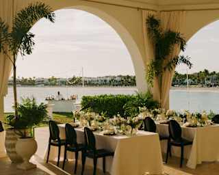 Two tables with white cloths and floral centrepieces await wedding guests in the event pavilion with stunning bay views.