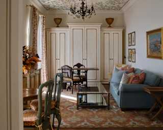 The living room exudes an old-world feel with green upholstered chairs, white wood cabinets, blue sofa and eclectic fabrics.