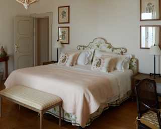 A tangle-design light pendant hangs above the bed, with soft pink throw and subtle floral cushions, in a view of the bedroom.