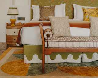 In a face-on view, an end-of-bed bench abuts a bed with an olive and white embroidered valance, complementing the headboard.