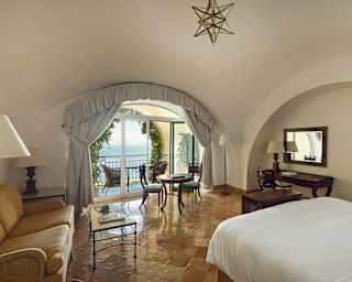 Sunlight plays across polished floor tiles while theatre-style curtains frame a glorious balcony view of the Tyrrhenian Sea