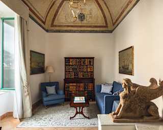 A Greek winged sphinx guards the entrance to a sitting room furnished with a sky blue sofa, armchair and bookcase