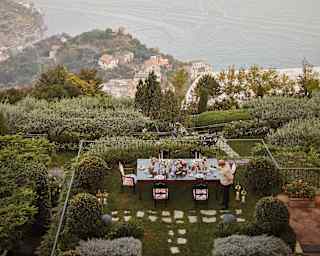 Outdoor table coated in flowers and candles overlooking lush hillside gardens