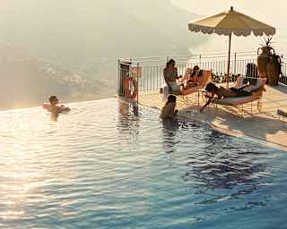 Two guests swim in the gold-tinted waters of the pool as they chat to three more who relax on loungers, seen from above.