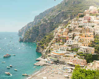 The peach-pastel buildings of Positano climb steep cliffs overlooking a busy beach and azure sea filled with pleasure boats.