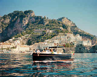 A group of friends enjoys a coastline tour aboard a beautiful black wooden boat as it cruises by pretty cliff-side towns.