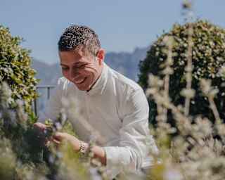 Chef Armando Aristarco wears long sleeve chef whites and smiles as he picks fresh oregano from the hotel gardens
