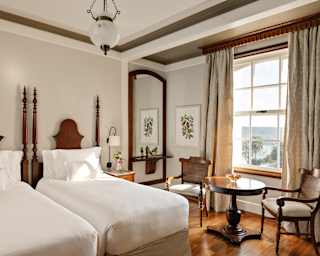 Window light illuminates a Deluxe Falls View room with crisp twin beds, polished floorboards and antique table and chairs.
