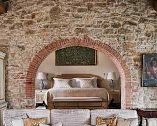 View through a rustic stone arch to the bedroom with double bed, luxury bedding and side tables, seen from the living area.