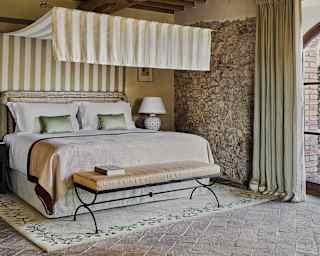 With a striped canopy, a large bed, with fabrics in natural tones, provides a restful corner in a room of cool, Tuscan stone.
