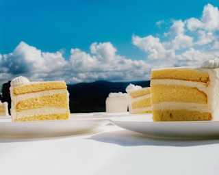 Eye-level view of a table where distant clouds create pretty puffs above plated slices of three-layer, cream-and-sponge cake.