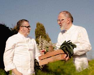 Tosca restaurant's Chef Daniele Sera holds a wooden crate of produce as he chats to another chef in the kitchen garden.