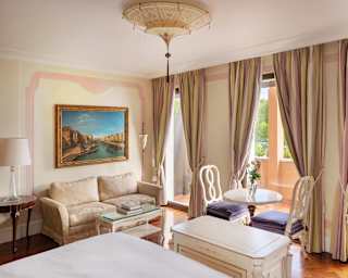 A refined bedroom with baroque furniture including a cream silk sofa. Neapolitan ice cream curtains frame full height windows