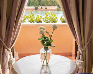 Curtains with Neapolitan ice cream stripes hang theatre-style before a large window, framing views of the lagoon