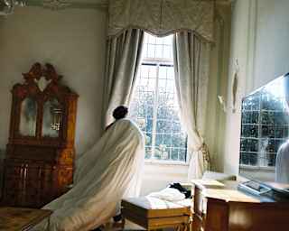 A guest, dragging a duvet, stands at a light-filled window in the Dogaressa Suite bedroom, gazing through the leaded panes.