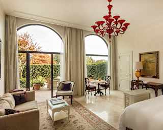 Open patio doors lead onto a private terrace encircled by tall hedges. Inside cabriole leg furniture sits on a marble floor
