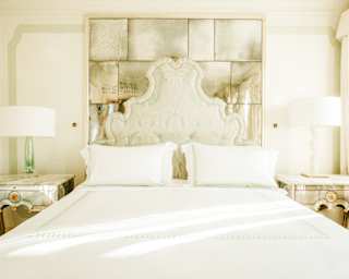 View from the foot of a white bed to a Rococo-style headboard and mirrored wall panel behind, seen in a bright Junior Suite.