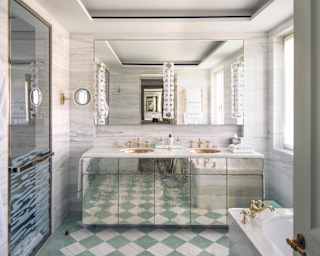 A silvery vanity unit reflects a green and white tiled floor and complements the grey marble of the Sophia Suite bathroom.