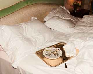 Four fresh oysters lie in a bowl of ice on a golden tray with two forks. The tray sits ready on a recently vacated bed