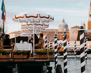 Hotel Cipriani guests dine al-fresco paraded by striped mooring poles with the Church of San Giorgio Maggiore rising behind.