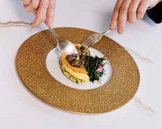 Two white porcelain bowls with intricate designs hold food and sit on shiny, round, gold-coloured tables with a reflective surface.
