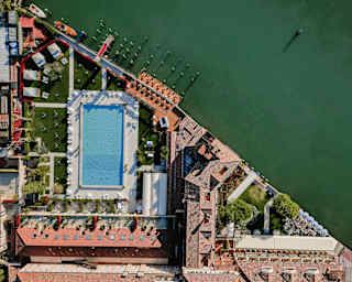 Birds-eye view of the rectangular sapphire-like pool, surrounded by terracotta rooftops and contrasting with the green canal.