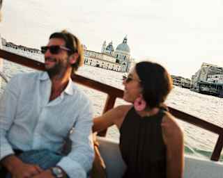 Tilted image of a man and woman in soft-focus as they relax on a boat, with the Basilica di Santa Maria della Salute crisp behind.