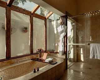 Sunlight plays above the Valley View bathroom windows in a view that captures a marble bath and shower areas, inside and out.