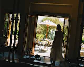 Angled image of a woman silhouetted in a casita doorway gazing at a sunny terrace outside, seen from a dark interior.