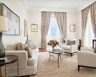 A chic sitting room, with modern monochrome furnishings, cream rug on a hardwood floor and dual aspect full height windows