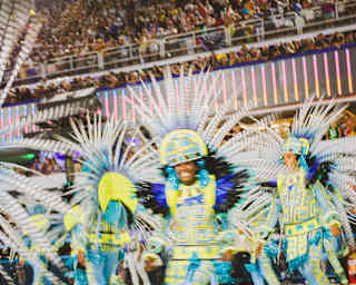 Carnival dancers, in flamboyant feather headdresses and yellow ad blue costumes, dance for an audience at the Sambadrome.