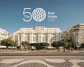 A grand hotel with white facade stands behind trees and a patterned pavement. Text above reads The 50 Best Hotels 2026.