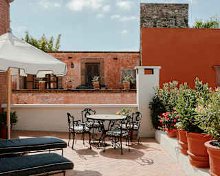On the terrace, lined with potted oleanders, two loungers and a parasol rest in shade as a table set takes a sunny corner.