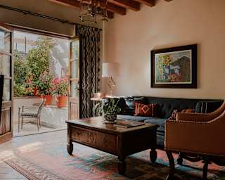 View over the living area where a teal sofa, leather armchair and wood coffee table enjoy the breeze from open terrace doors.