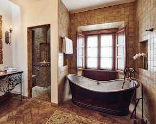 A copper bateau bathtub soaks in light by the window in a tiled Studio Suite bathroom with walk-in shower and vanity table.