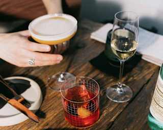 A hand reaches for an espresso martini at a table with a Negroni, a flute of sparkling wine and a plate of unctuous seafood.