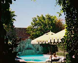 A guest relaxes on a chair by the sparkling pool in the hotel's walled garden, seen through an arch clad with climbers.